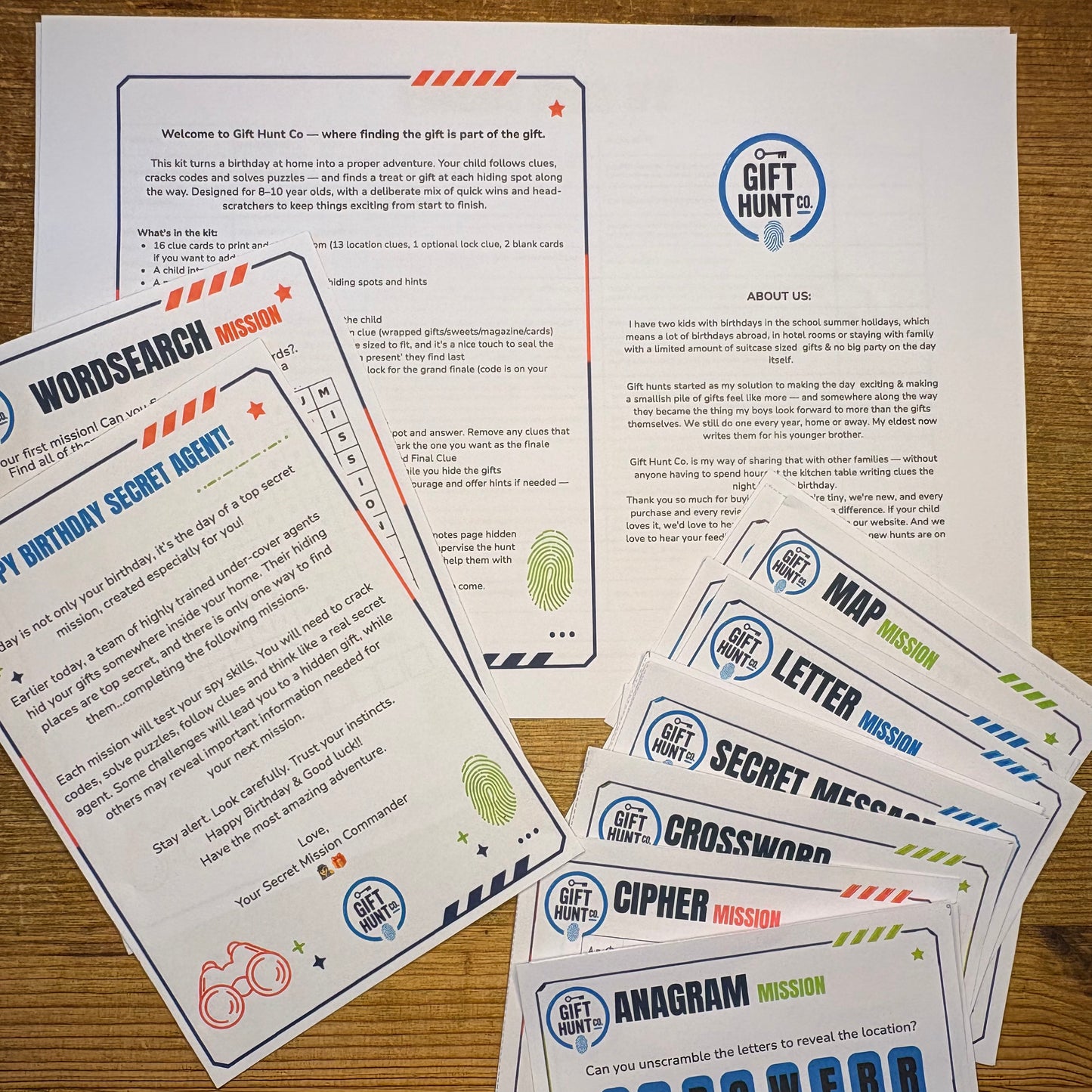 A set of printed gift hunt game cards and a welcome sheet laid out on a wooden surface. The cards include missions such as Word Search, Letter, Cipher, Crossword, and Amagram, with printed text and colorful blue, orange, green, and red accents.